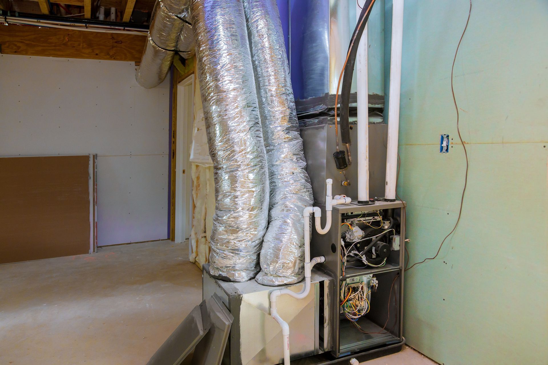 HVAC unit with ductwork in a basement. Silver insulated ducts, white pipes, beige and green walls.