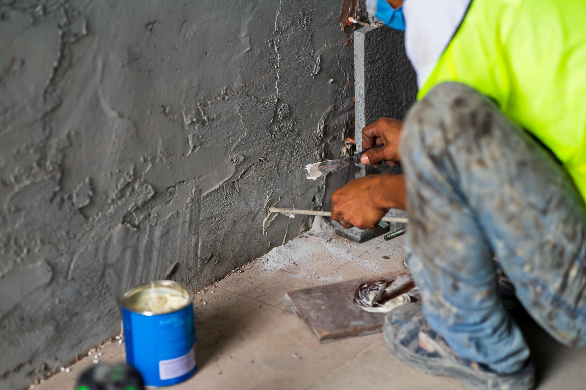 Construction worker applying stucco to a wall; wearing a safety vest.