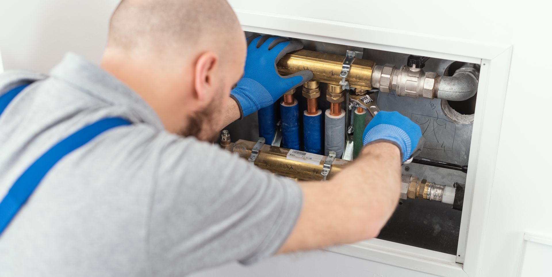 Plumber wearing blue gloves working on pipes inside a white box.