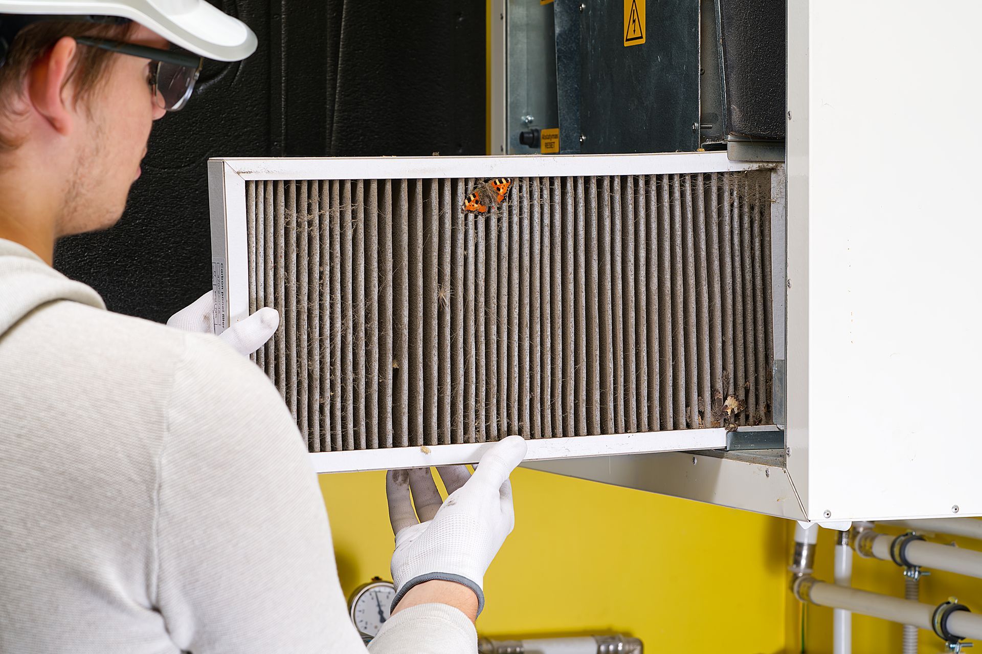 Person wearing gloves removing a very dirty air filter from a furnace.