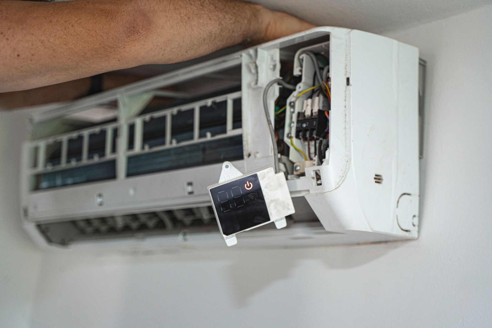 A person repairs a white wall-mounted air conditioner, opening the unit to access internal components.