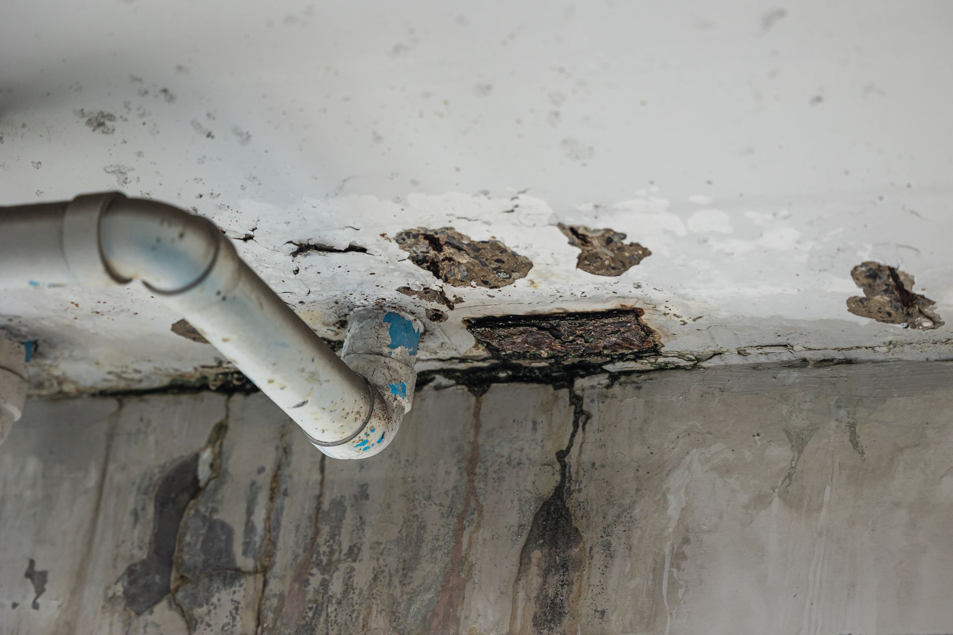 Damaged ceiling with holes and exposed concrete, near a white pipe.