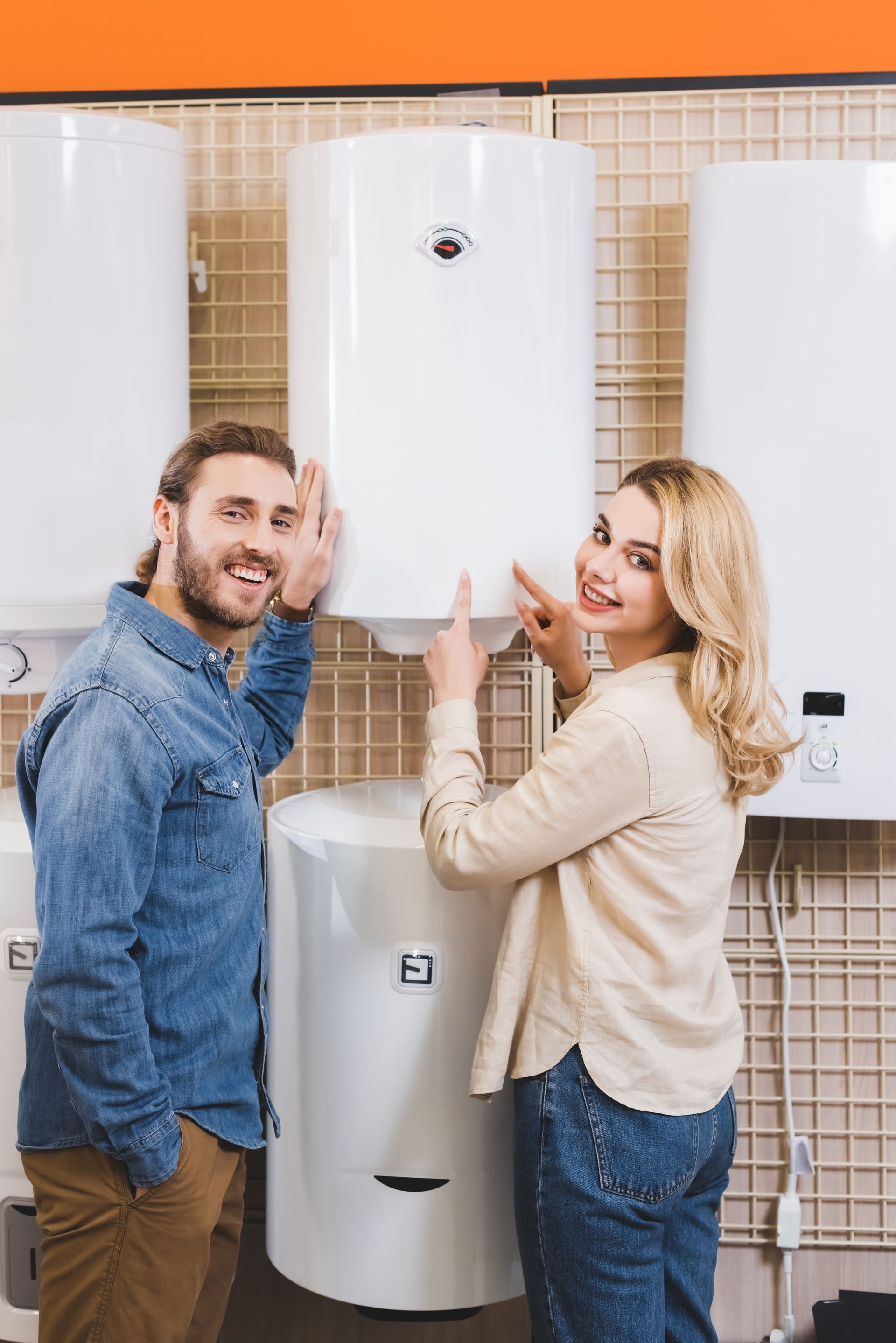 Couple in a hardware store examining a white water heater, smiling and pointing.