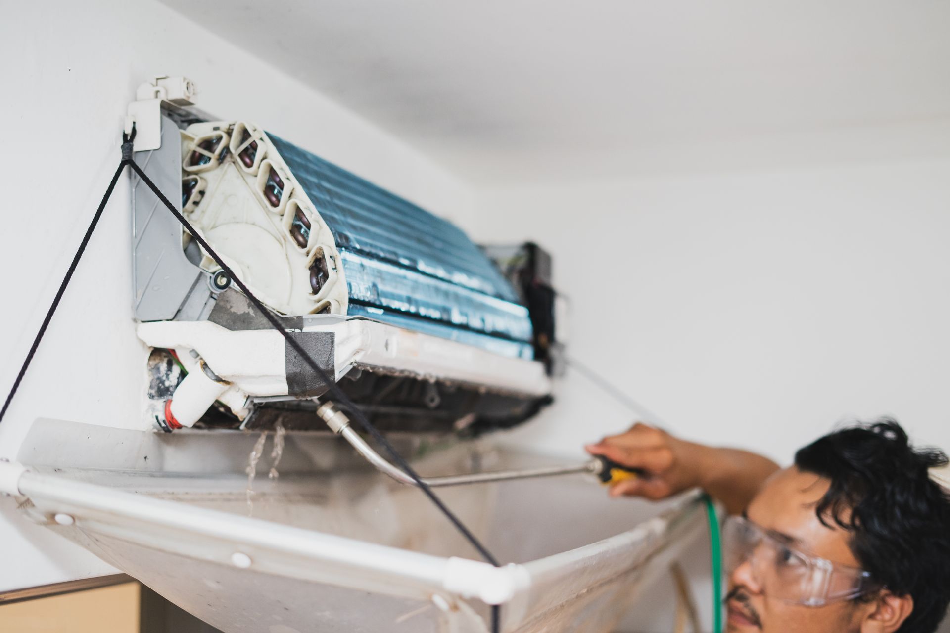 Man cleaning a wall-mounted air conditioner with a protective cover.