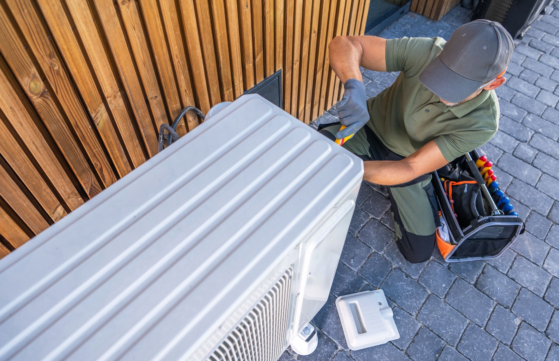 HVAC technician in green uniform repairing air conditioner unit outdoors.