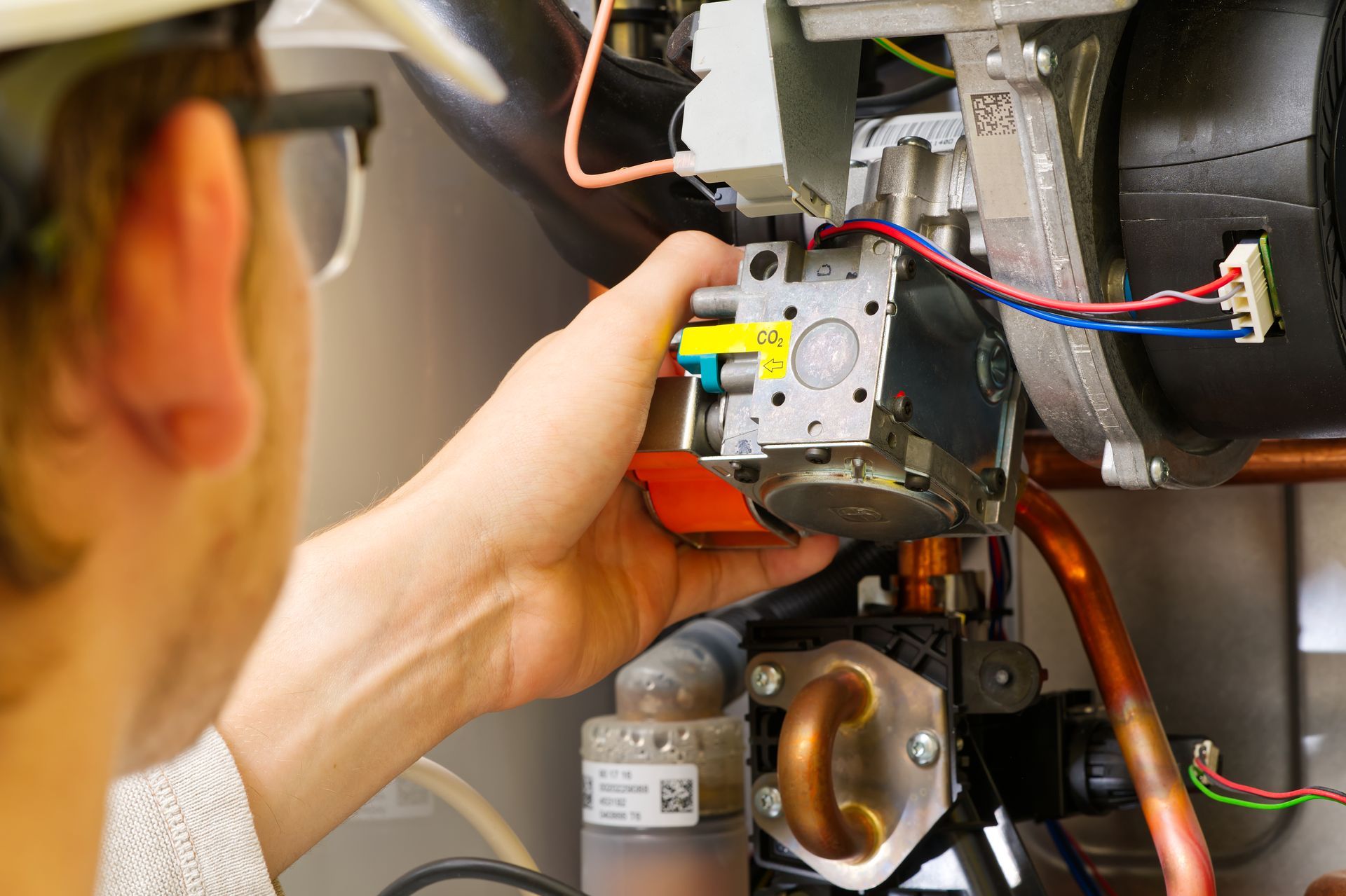 A technician in a hard hat repairs a furnace, examining components with focused attention.