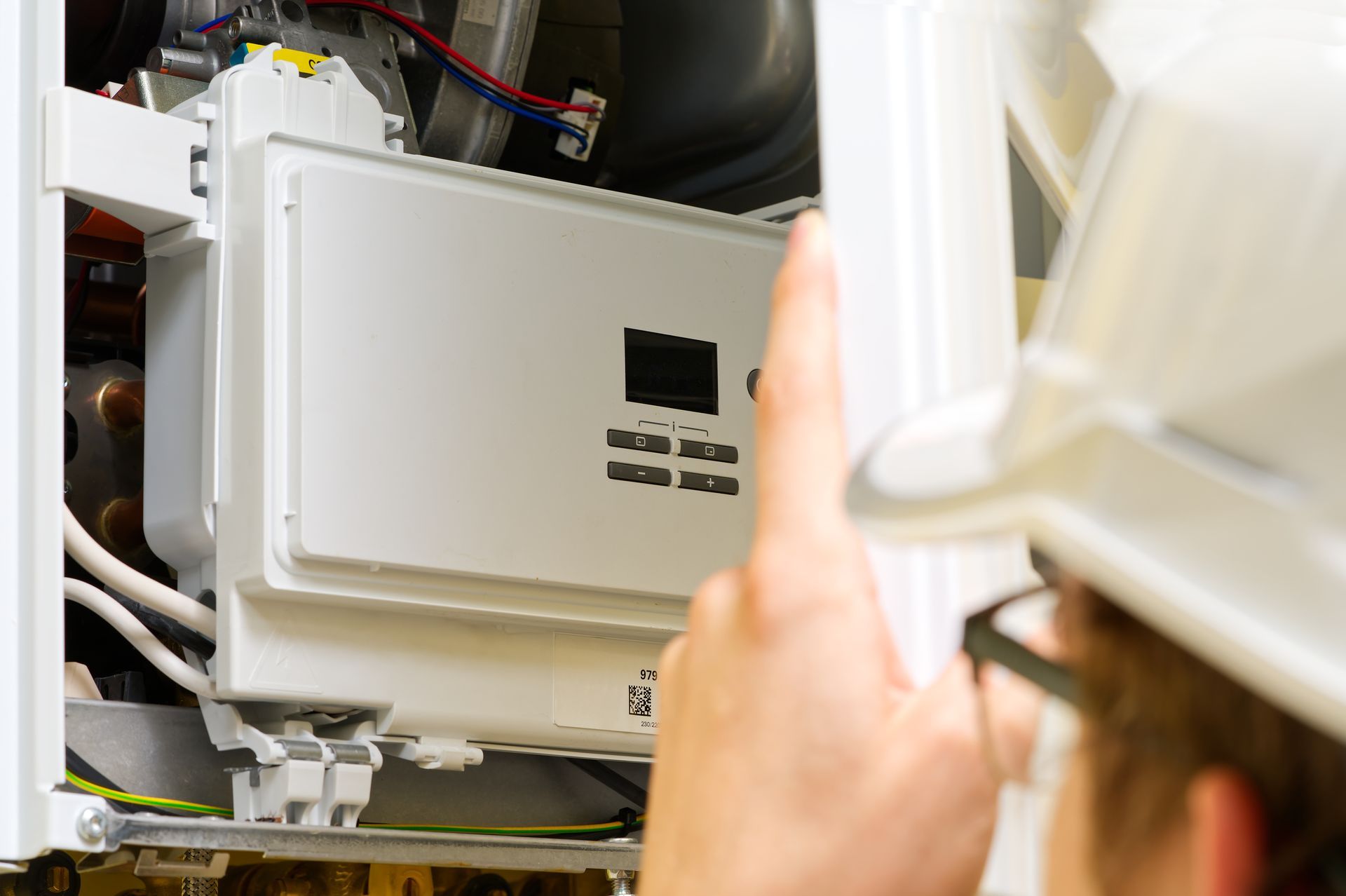 Person wearing a hard hat pointing at a white appliance, likely a boiler or furnace.