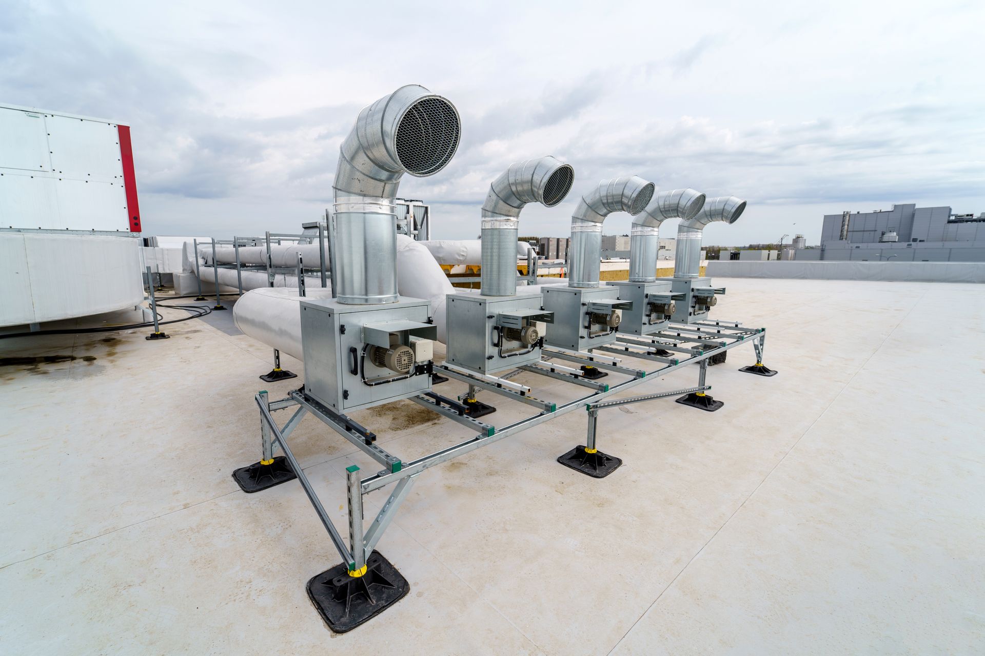 Rooftop HVAC equipment, including ducts and vents, on a flat, white-surfaced roof. Gray sky in background.