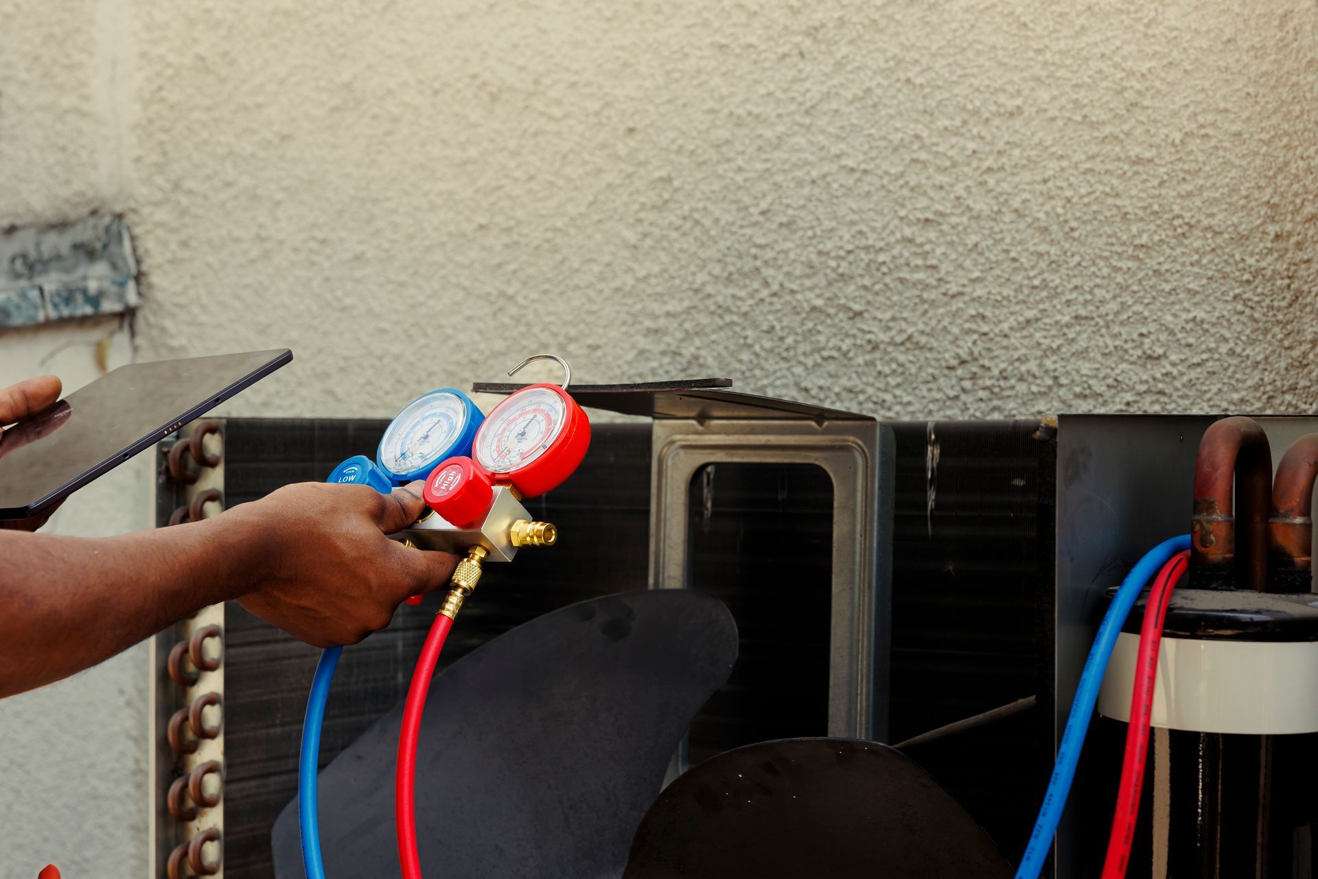 AC technician connecting gauges to an outdoor unit, checking refrigerant pressure.