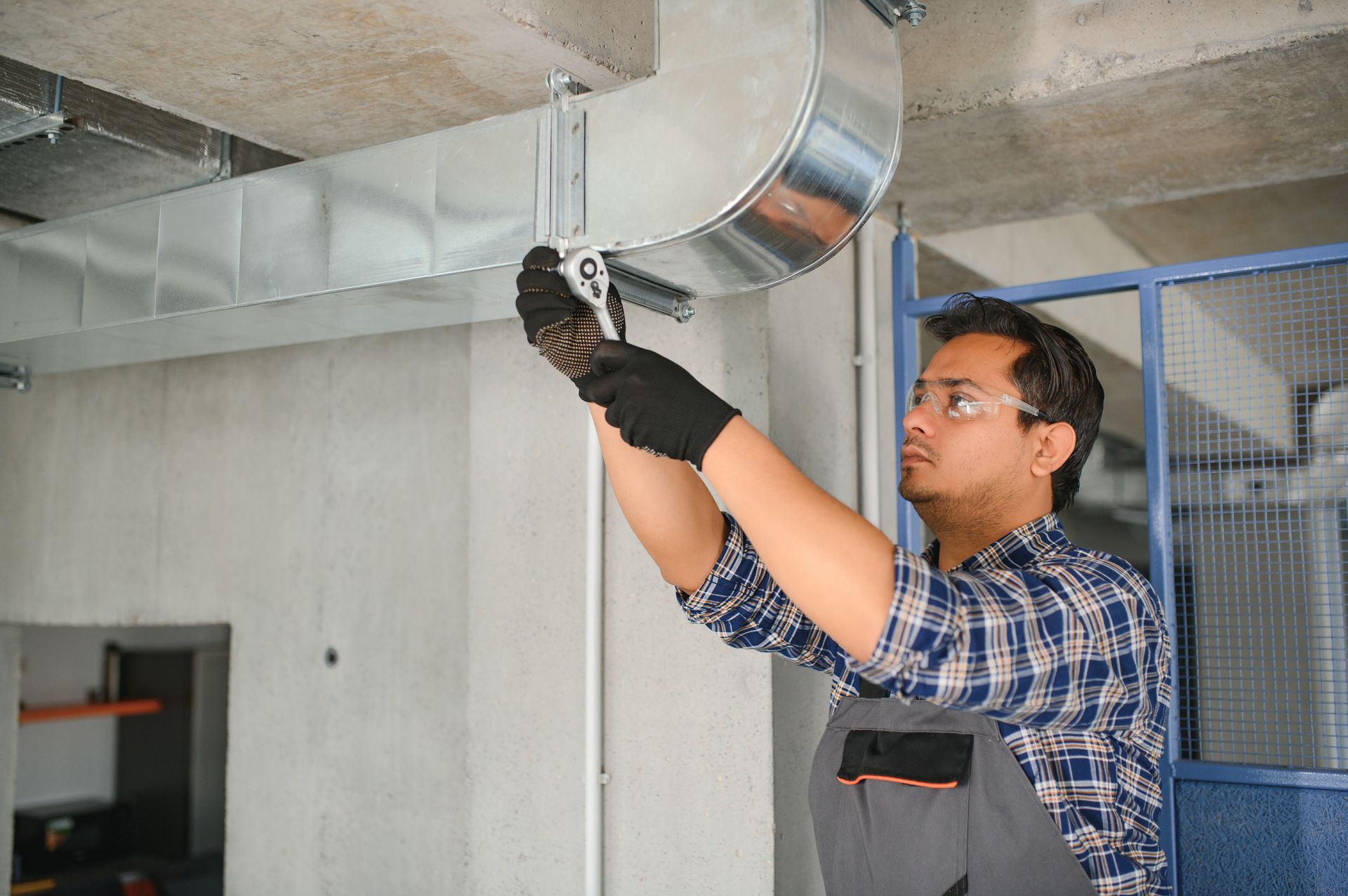 Man in safety glasses and gloves installs ventilation ductwork with a wrench.