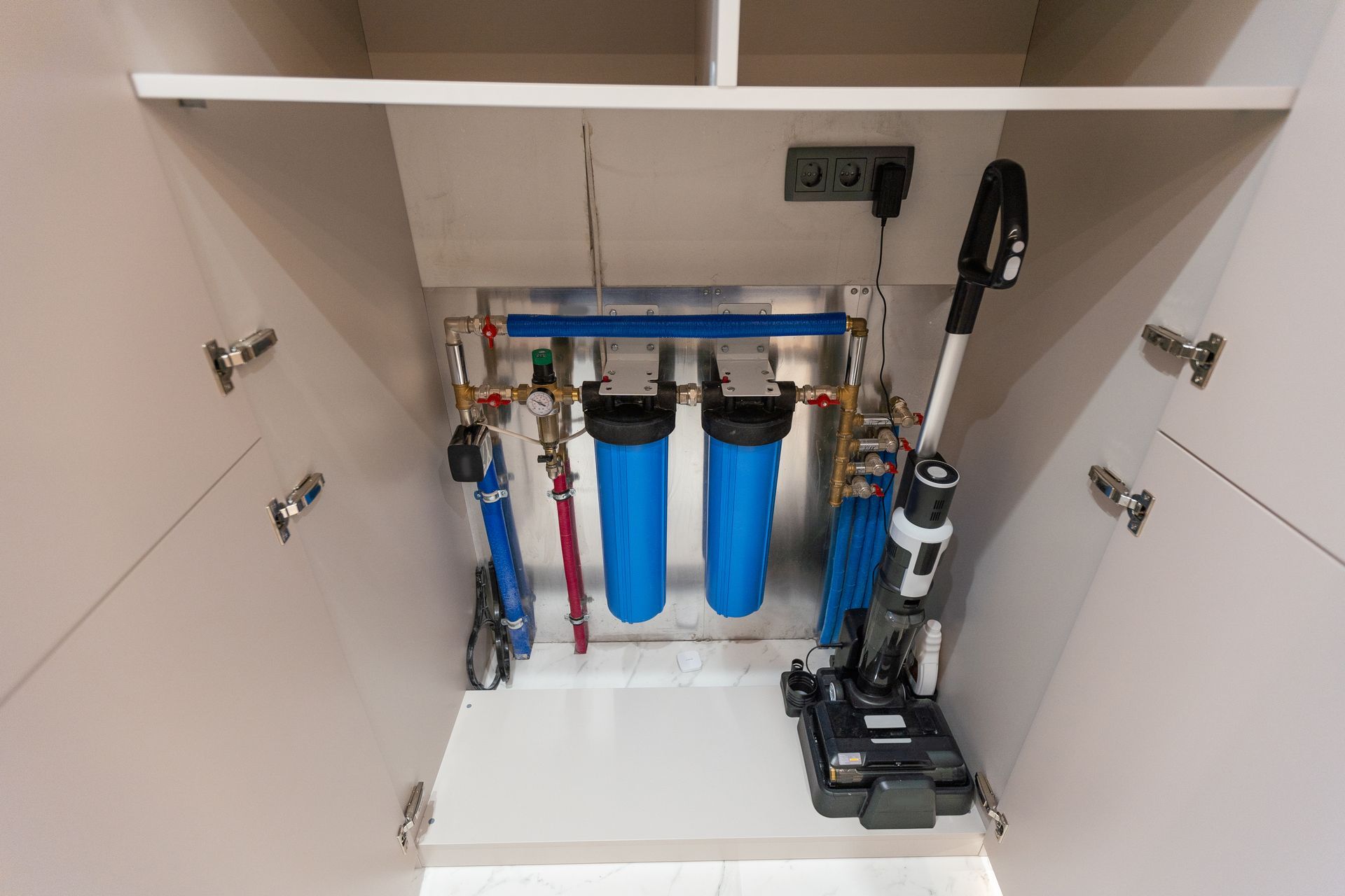 Inside a cabinet: water filters, vacuum cleaner, and storage for hoses and attachments.