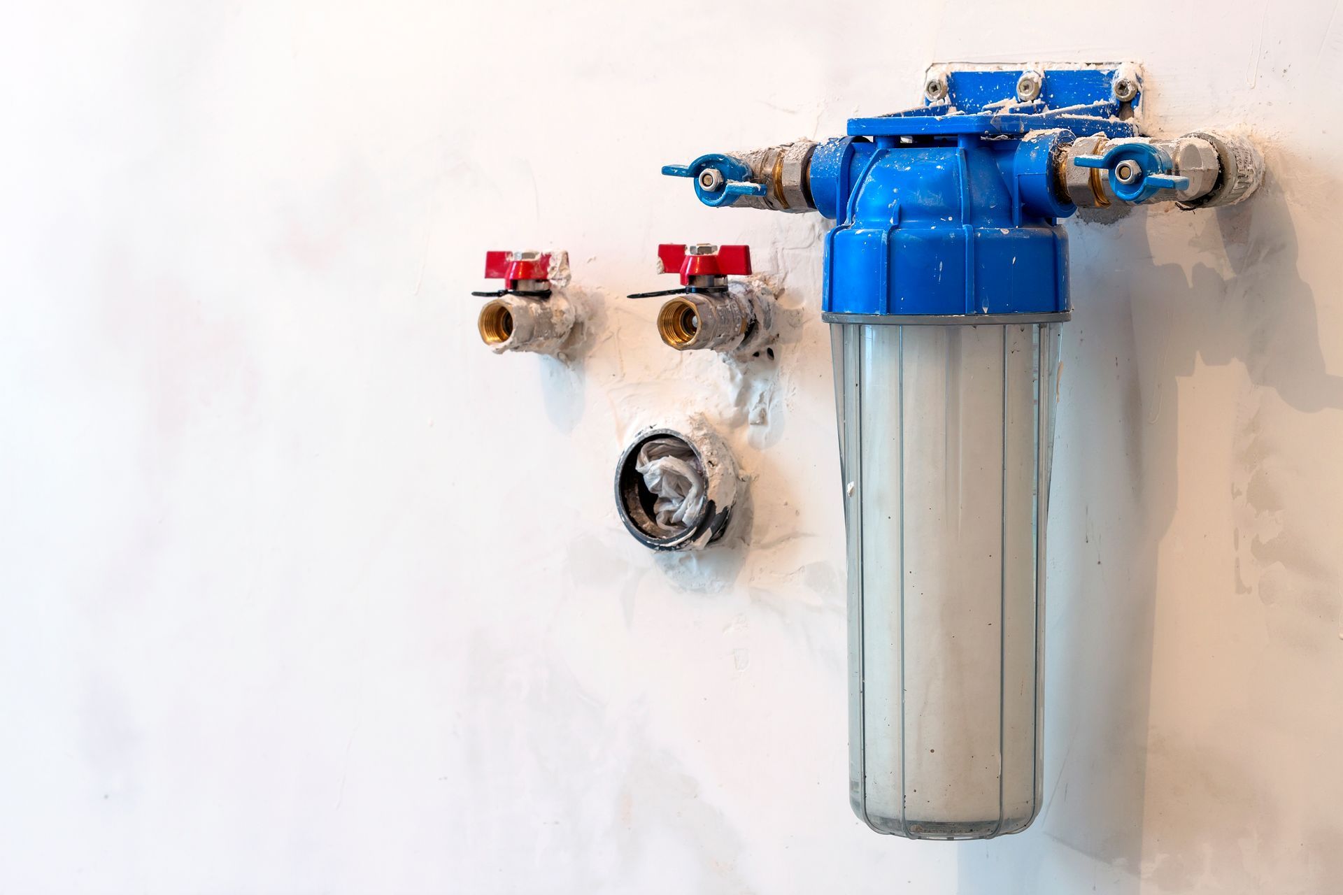 Blue and white water filter system attached to a white wall with red valves.