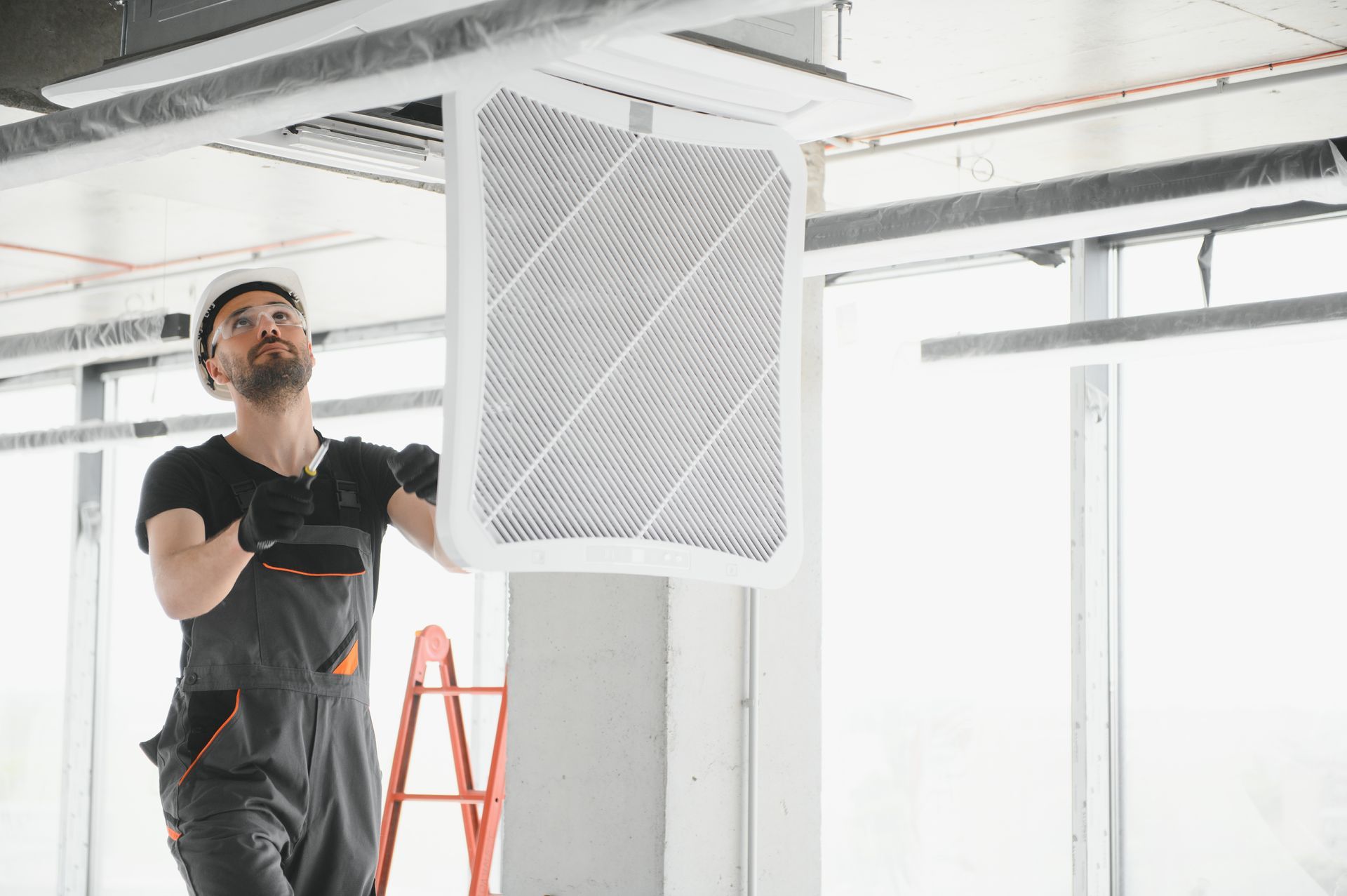 Construction worker in hard hat installs ceiling vent in unfinished building.