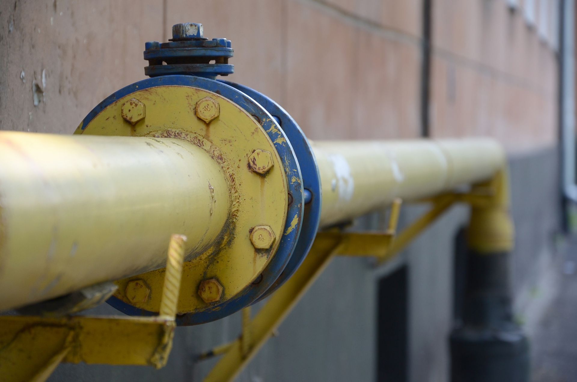 Yellow gas pipe bolted to a building, with blue flanges and rust.