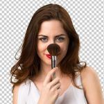 A woman is holding a makeup brush in front of her face.