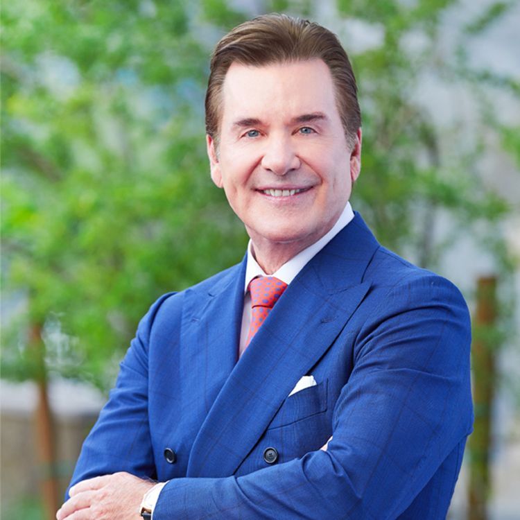 A man in a blue suit and red tie is smiling with his arms crossed.
