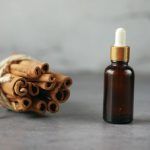 A bottle of essential oil next to a bunch of cinnamon sticks.