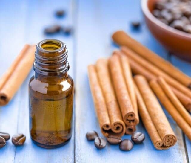 A bottle of essential oil next to cinnamon sticks and coffee beans