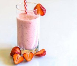 A strawberry smoothie in a glass with strawberries on the side.