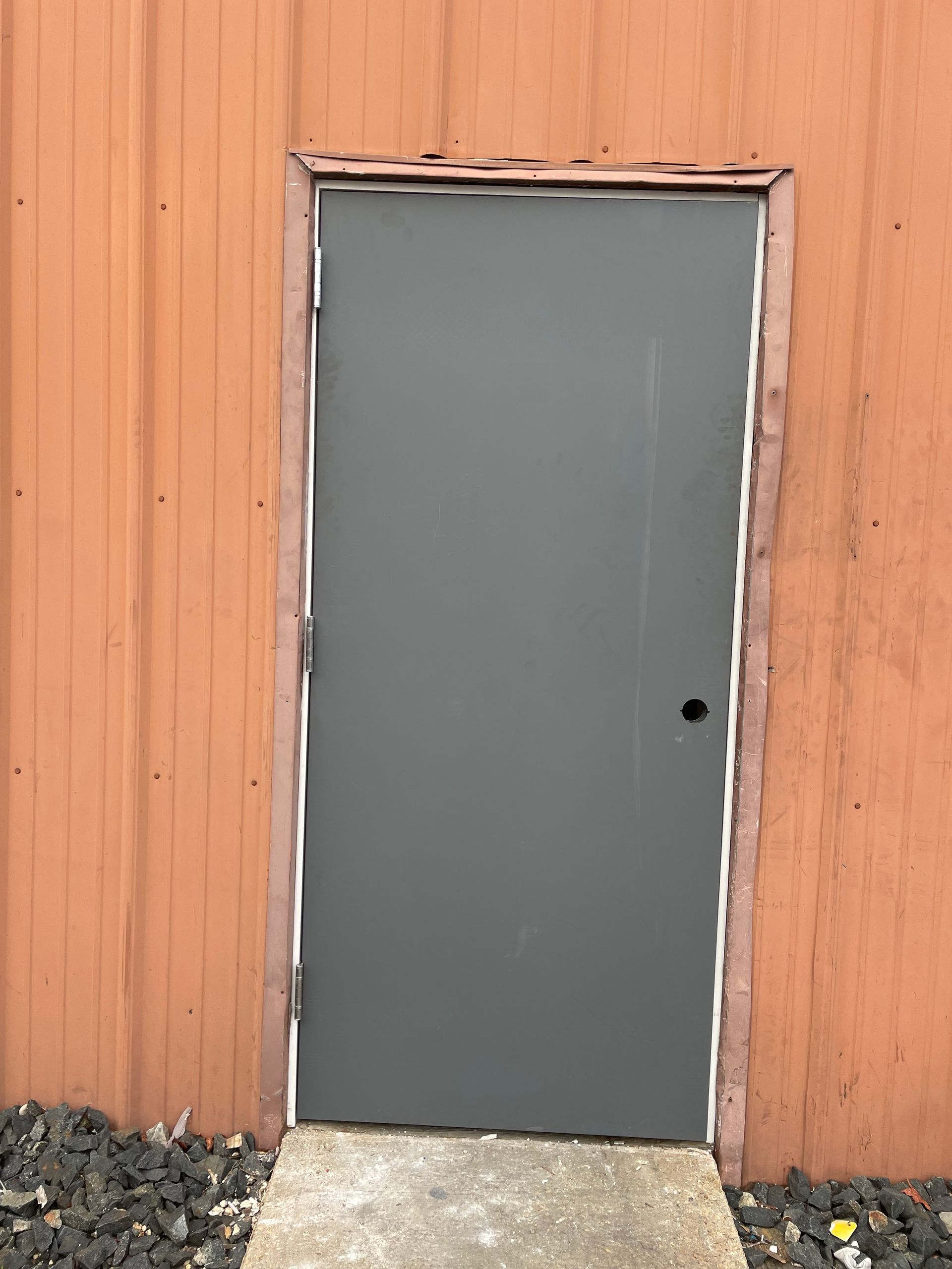 A gray door with a wooden frame is against an orange wall