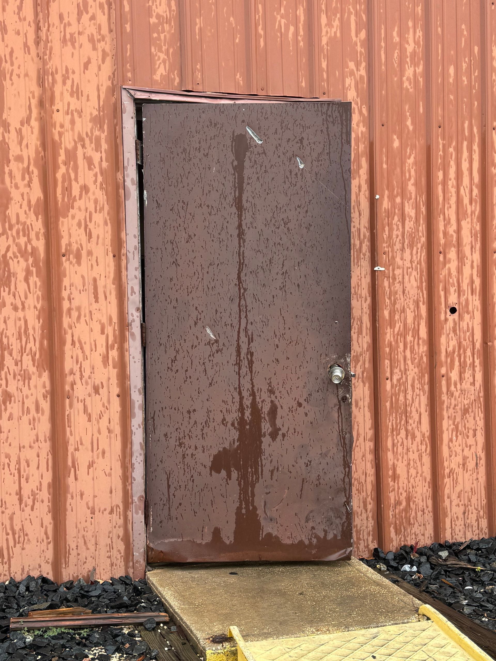 A rusty door on a building with a ramp in front of it