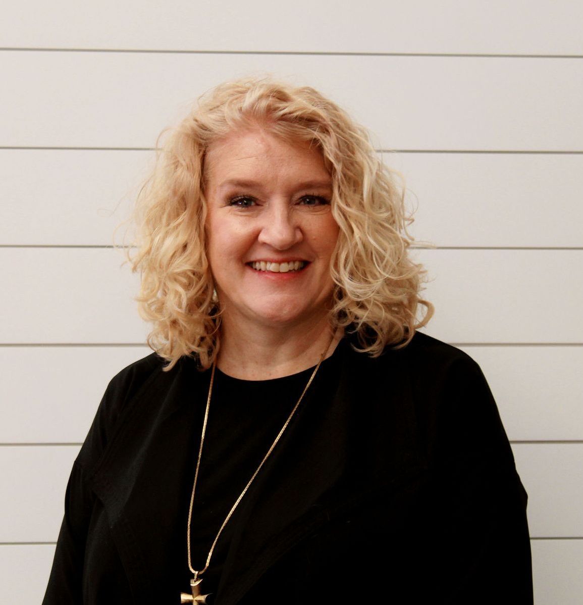 A woman wearing a black shirt and a necklace is smiling.