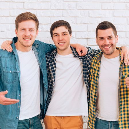 Three young men are posing for a picture in front of a white brick wall.
