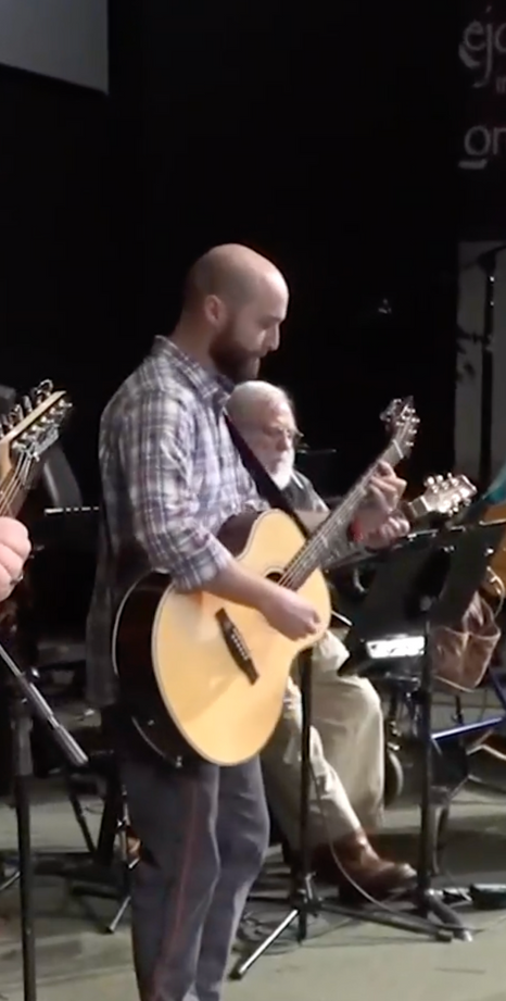 A man is playing an acoustic guitar in a band