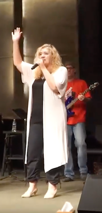 A woman is singing into a microphone on a stage.