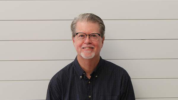 A bald man with a beard is wearing a blue shirt and smiling for the camera.