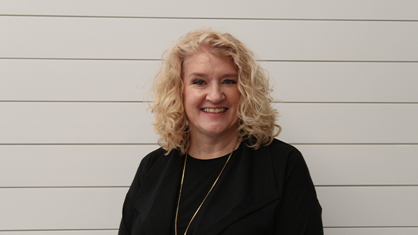 A woman wearing a black shirt and a necklace is smiling.