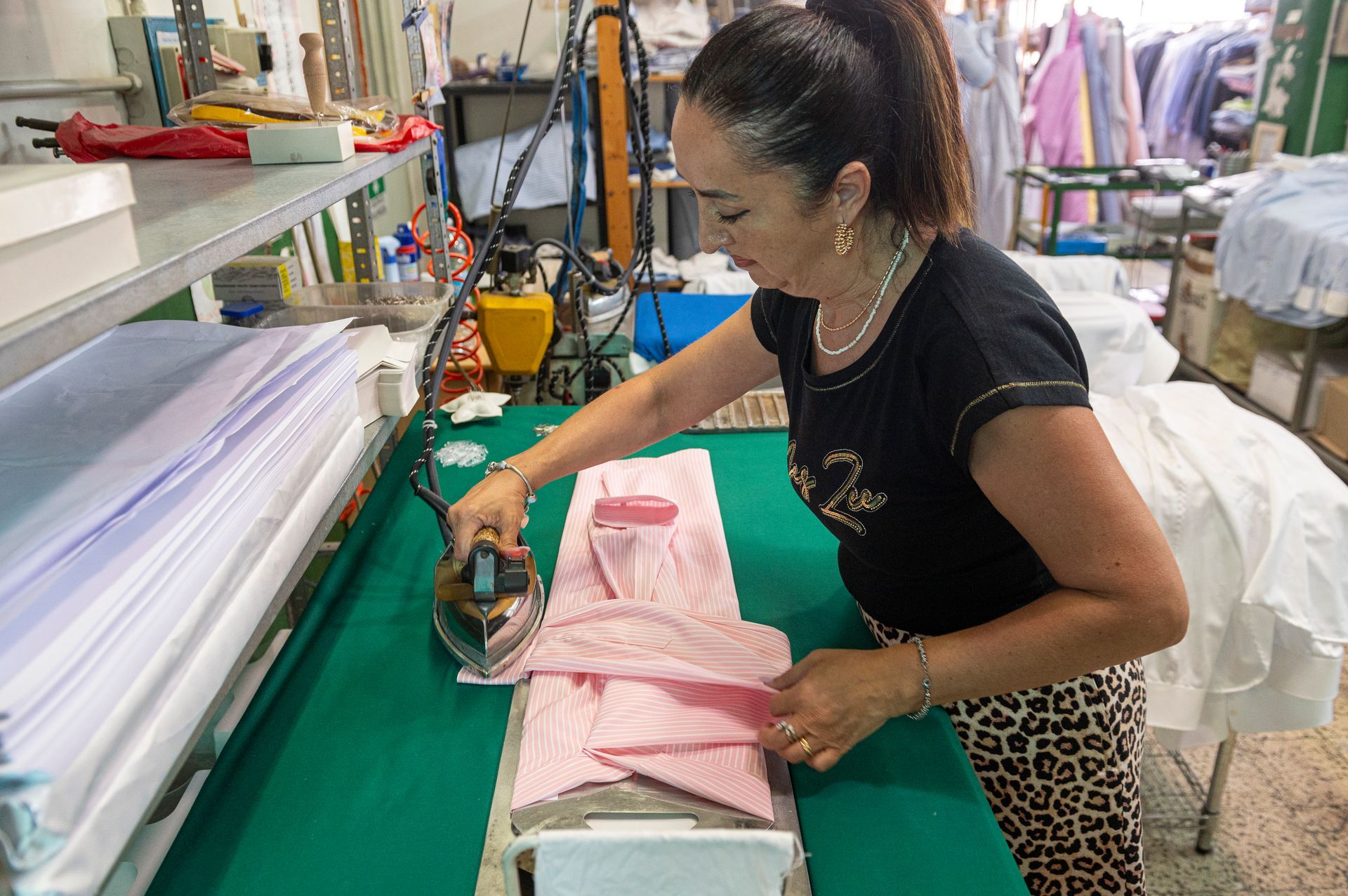 Una donna sta stirando una camicia rosa su un tavolo verde.