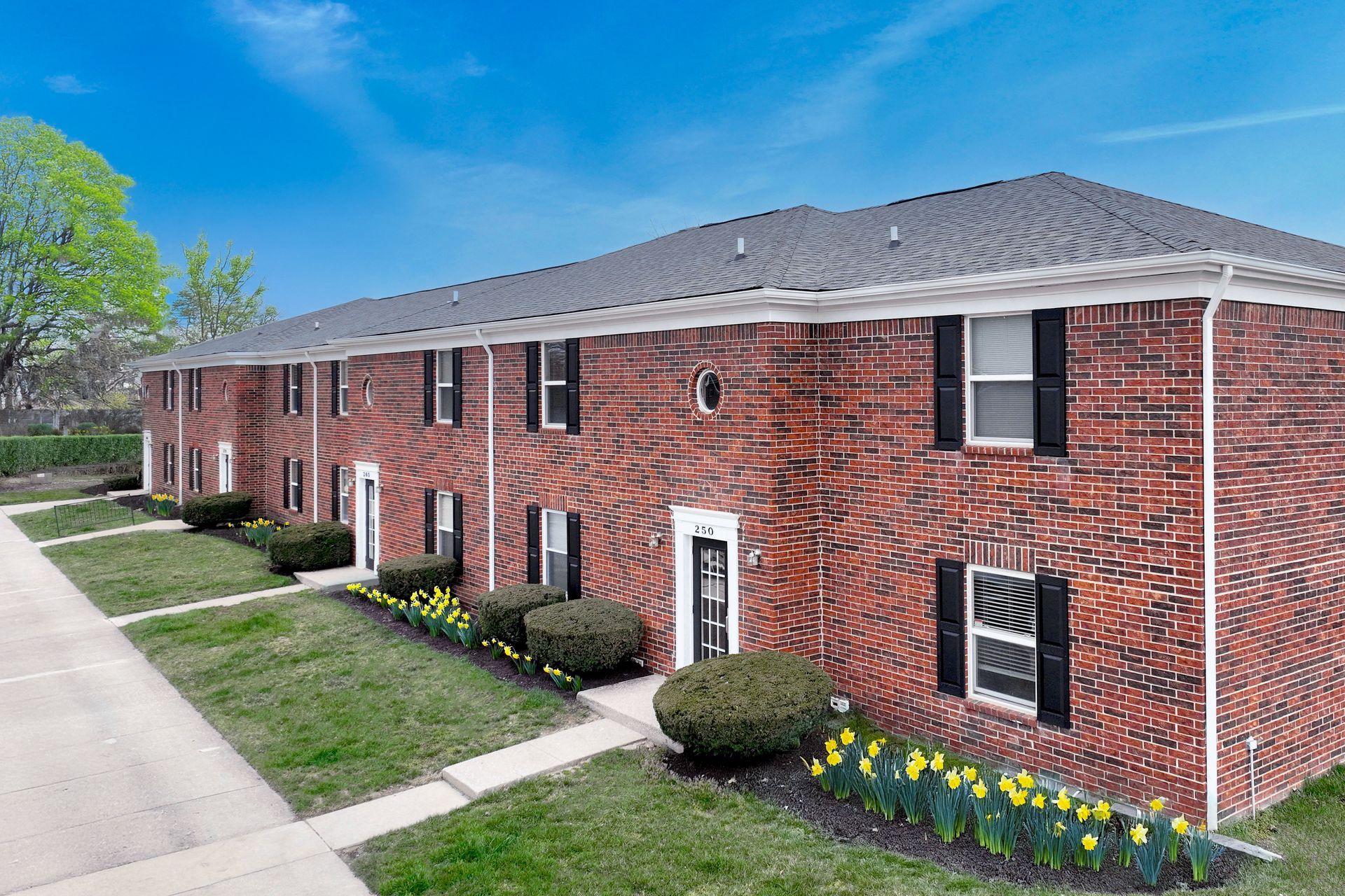 A large brick apartment building with a lush green lawn in front of it.