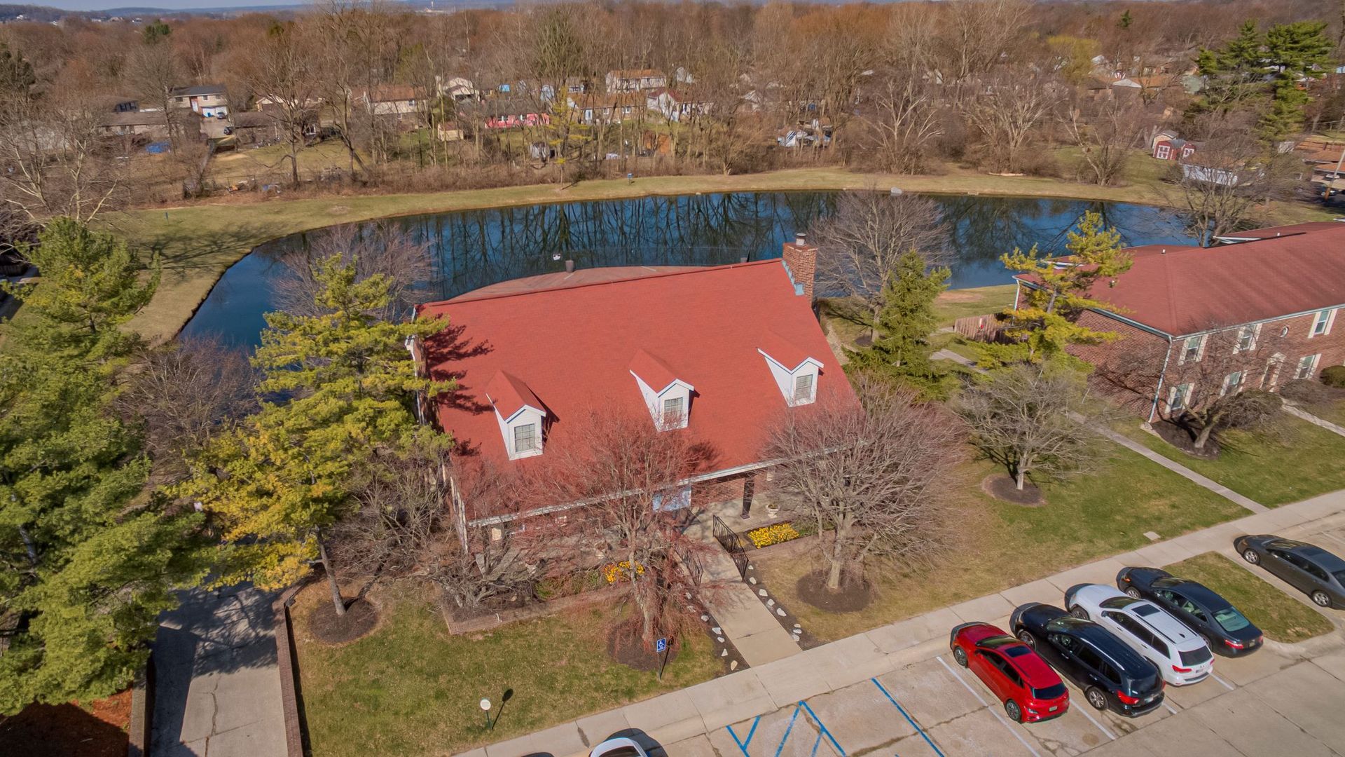 An aerial view of a clubhouse with a red roof and a lake in the background.
