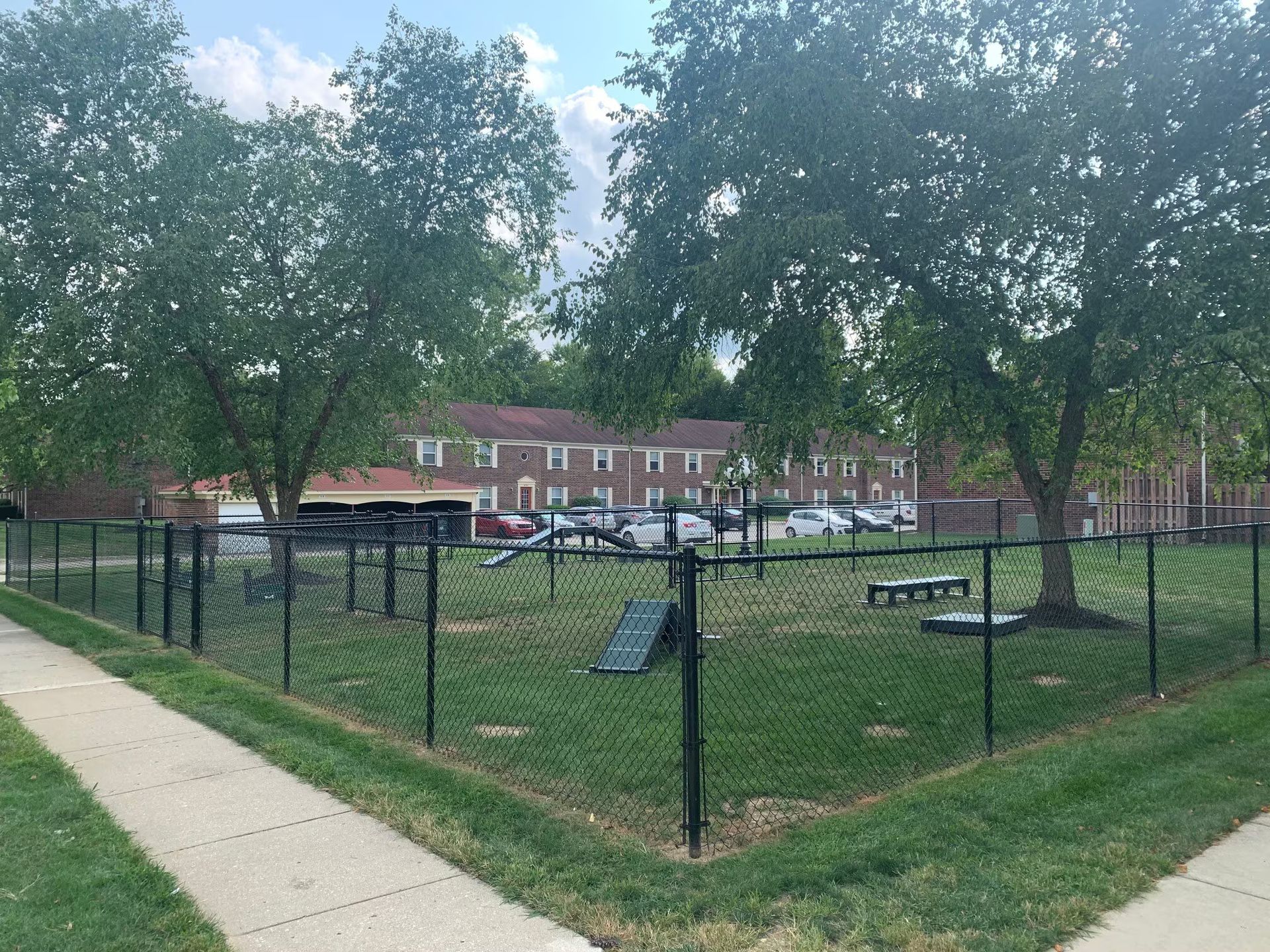 A dog park is surrounded by a chain link fence and a sidewalk.