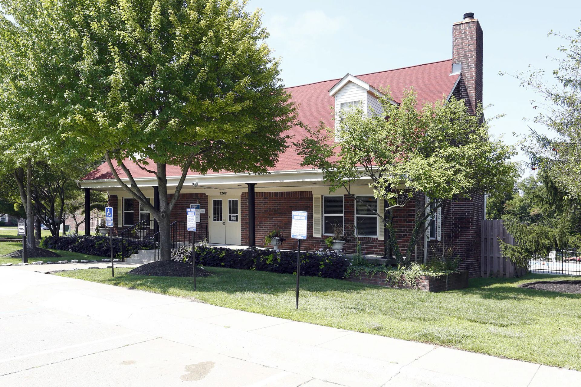A brick house with a red roof is surrounded by trees.