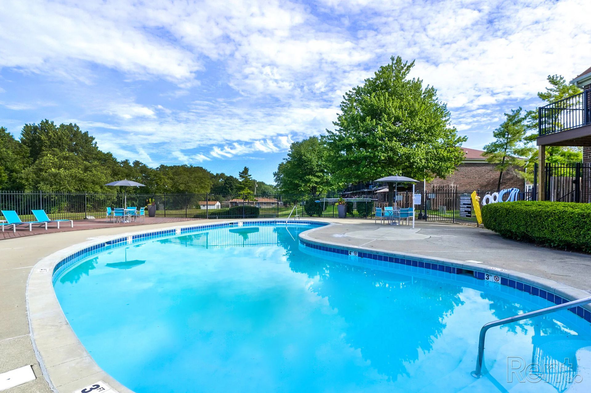 A large swimming pool surrounded by chairs and trees on a sunny day.