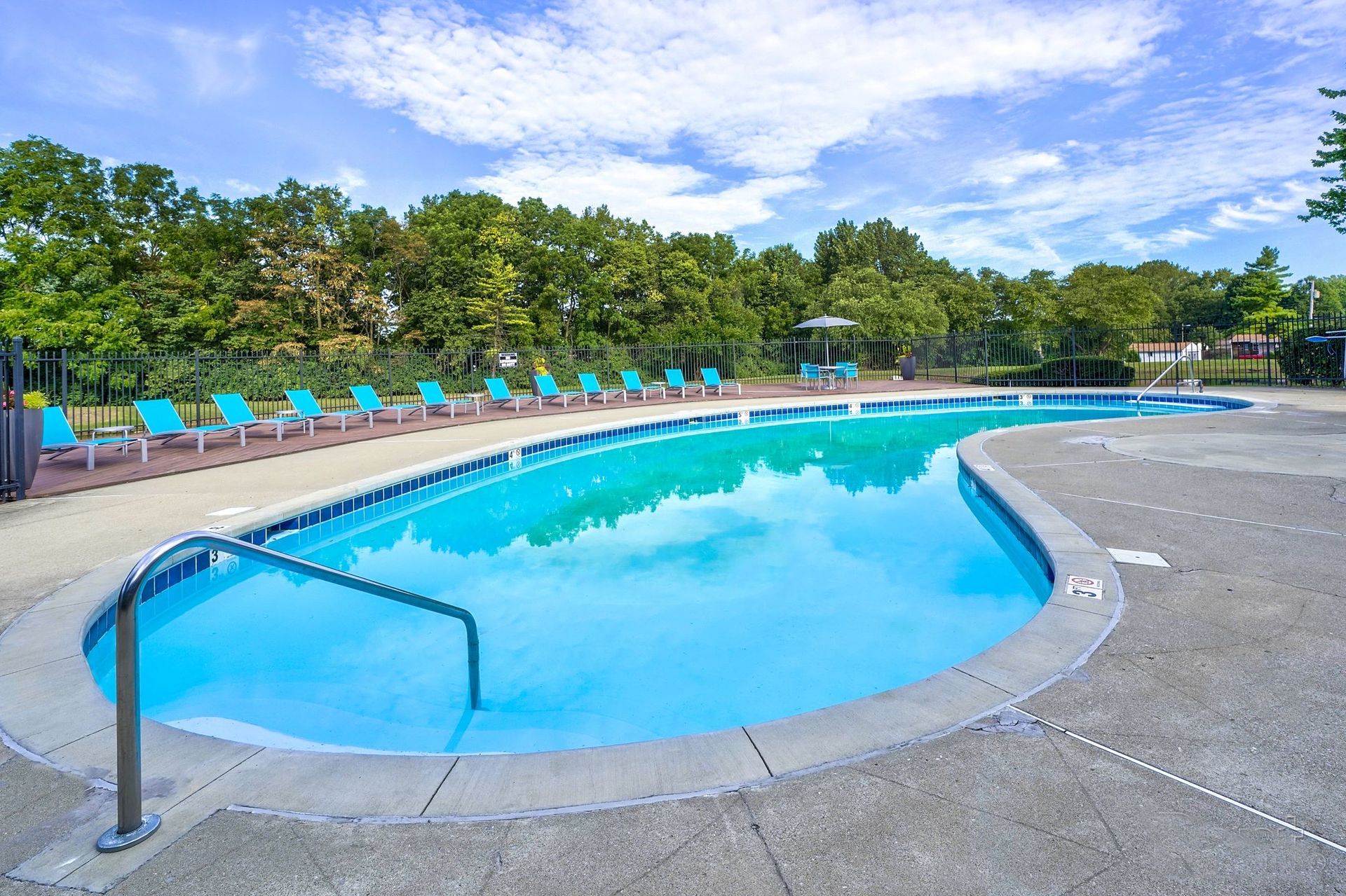 A large swimming pool surrounded by chairs and trees on a sunny day.