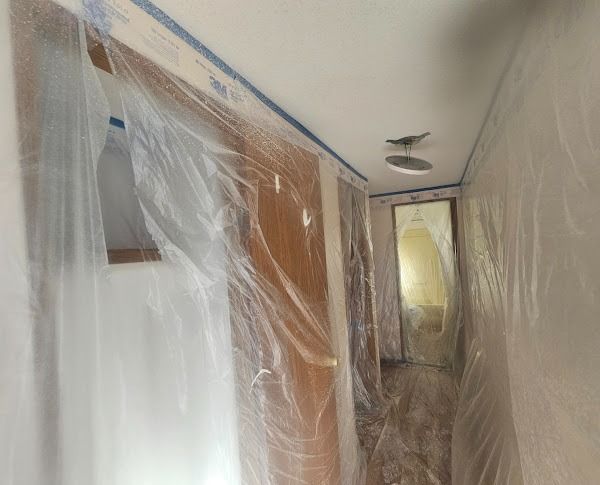 Hallway under renovation, plastic sheeting taped to walls and ceiling for protection.