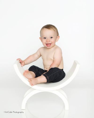 Smiling baby sitting on white arched bench, looking at the viewer.