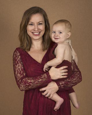 Woman in red dress holds smiling baby, both looking at the camera.