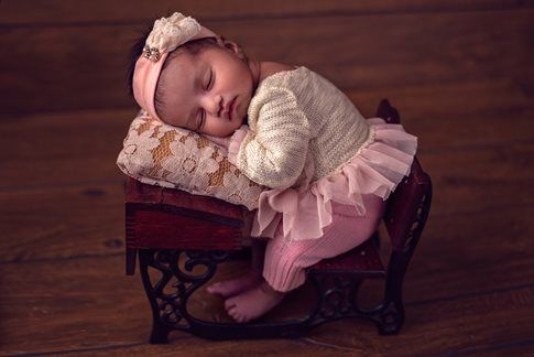 Newborn sleeps on a tiny sewing machine, wearing pink tutu and headband.