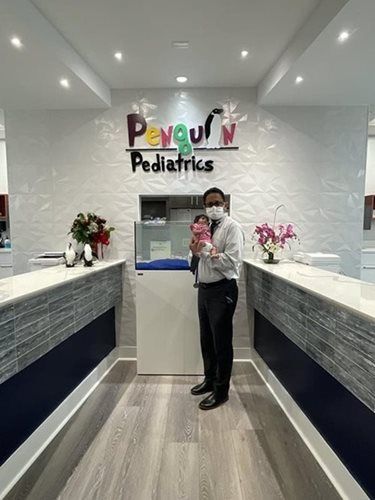 Man in a white shirt and tie holding a baby in a pediatric office. 