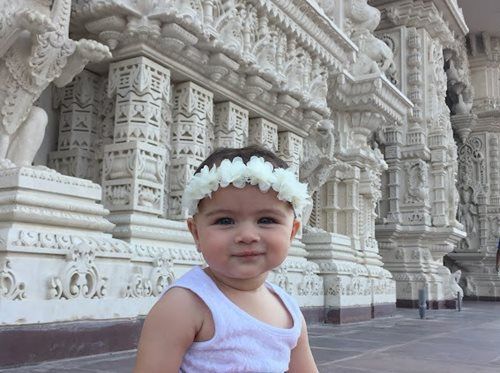 Child wearing floral crown in front of intricately carved white building, smiling.