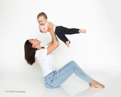 Woman lifting a baby in the air against a white backdrop; both smiling.