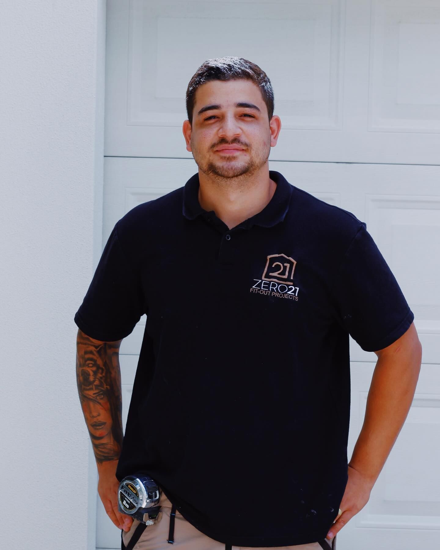 Man in black polo shirt stands in front of a white garage door, holding a measuring tape. — Zero 21 Fit-Outs & Joinery: Kitchen Renovation Gold Coast In Molendinar, QLD