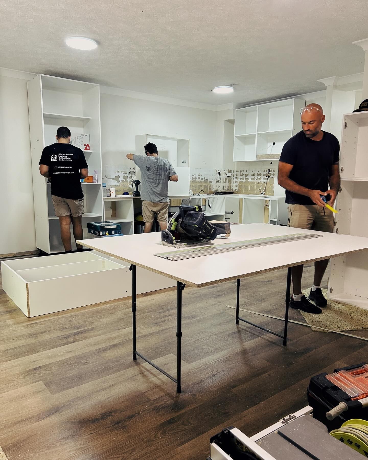 Three men assemble shelving in a white-walled room with wood-look floors.  — Zero 21 Fit-Outs & Joinery: Kitchen Renovation Gold Coast in Molendinar, QLD