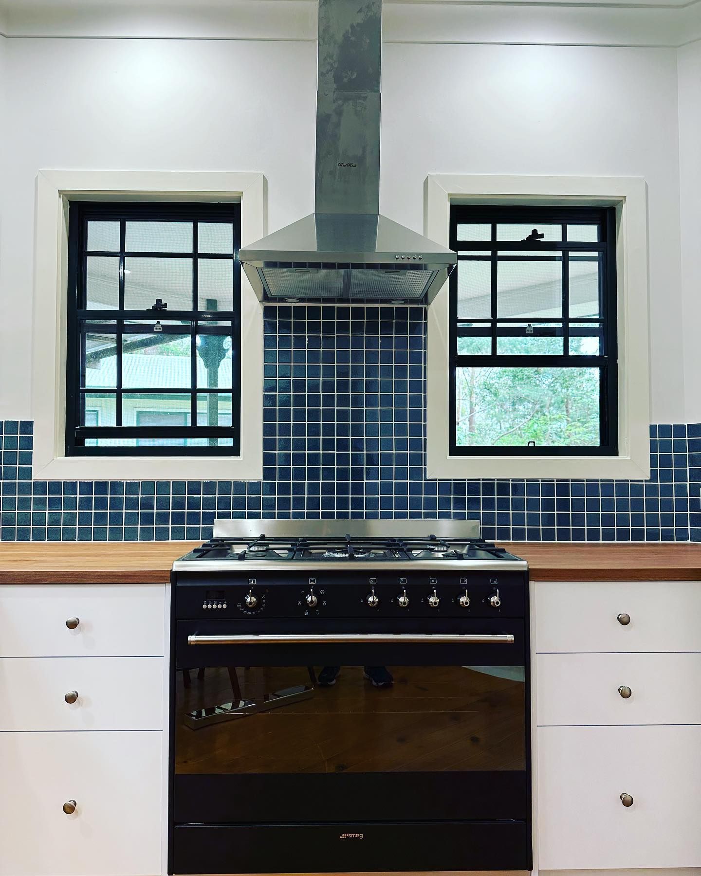 Kitchen with a black range, blue tiled backsplash, white cabinets, and windows. — Zero 21 Fit-Outs & Joinery: Kitchen Renovation Gold Coast in Paradise Point, QLD