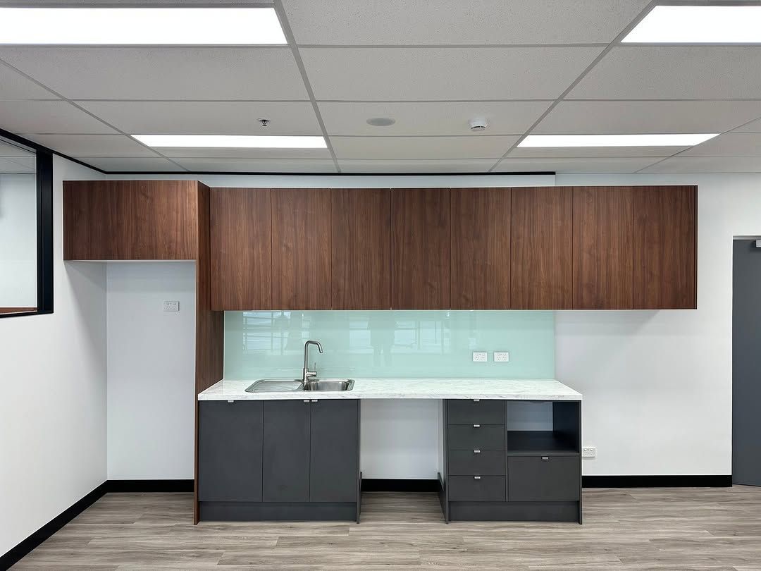 A small office kitchenette: dark wood cabinets, gray lower cabinets, light blue backsplash, and a sink. — Zero 21 Fit-Outs & Joinery: Kitchen Renovation Gold Coast in Robina, QLD