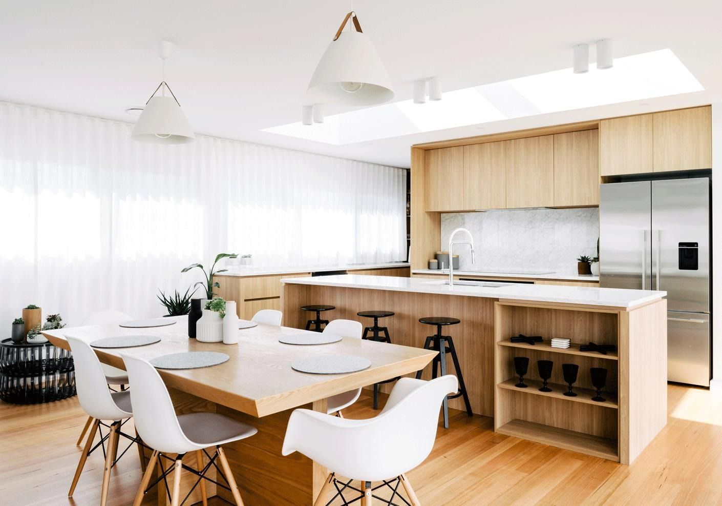 Modern kitchen and dining area with light wood cabinets, island, and table, white chairs, stainless steel fridge, and skylight. — Zero 21 Fit-Outs & Joinery: Kitchen Renovation Gold Coast in Burleigh Heads, QLD